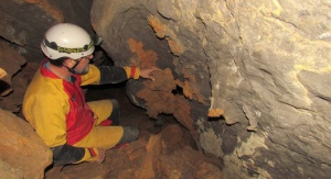 Relikty dedolomitu (pomarańczowe fragmenty na ścianach) w jaskini Mravljeto brezno v Gošarjevih rupah w Słowenii (na fotografii jeden z uczestników projektu HYPOCAVE, prof. Armstrong Osborne z Uniwersytetu w Sydney). Fot. Andrzej Tyc