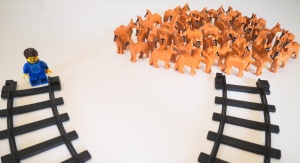 Zdjęcie ilustrujące dylemat wagonika. Mężczyzna i grupa psów z klocków LEGO stoi  koło torów kolejowych | fot. Mariola Paruzel-Czachura