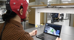 mężczyzna w czerwonym czepku z czujnikami patrzy na monitor komputera, na którym widać grę wyścigową