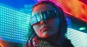 Kobieta z krótkimi włosami ma na oczach futurystyczne okulary zasłaniające oczy. Za nią ściana z neonami