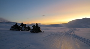 Naukowcy na skuterach śnieżnych na lodowcu Hansa na tle zachodzącego słońca | fot. Michał Laska