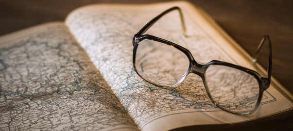 okulary leżące na starej książce z mapami