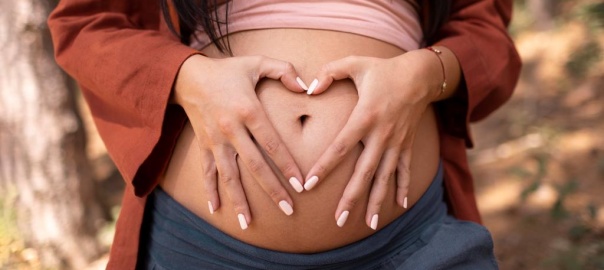 Brzuch kobiety w ciąży. Palce układa na brzuchu w kształcie serca | fot. Freepik
